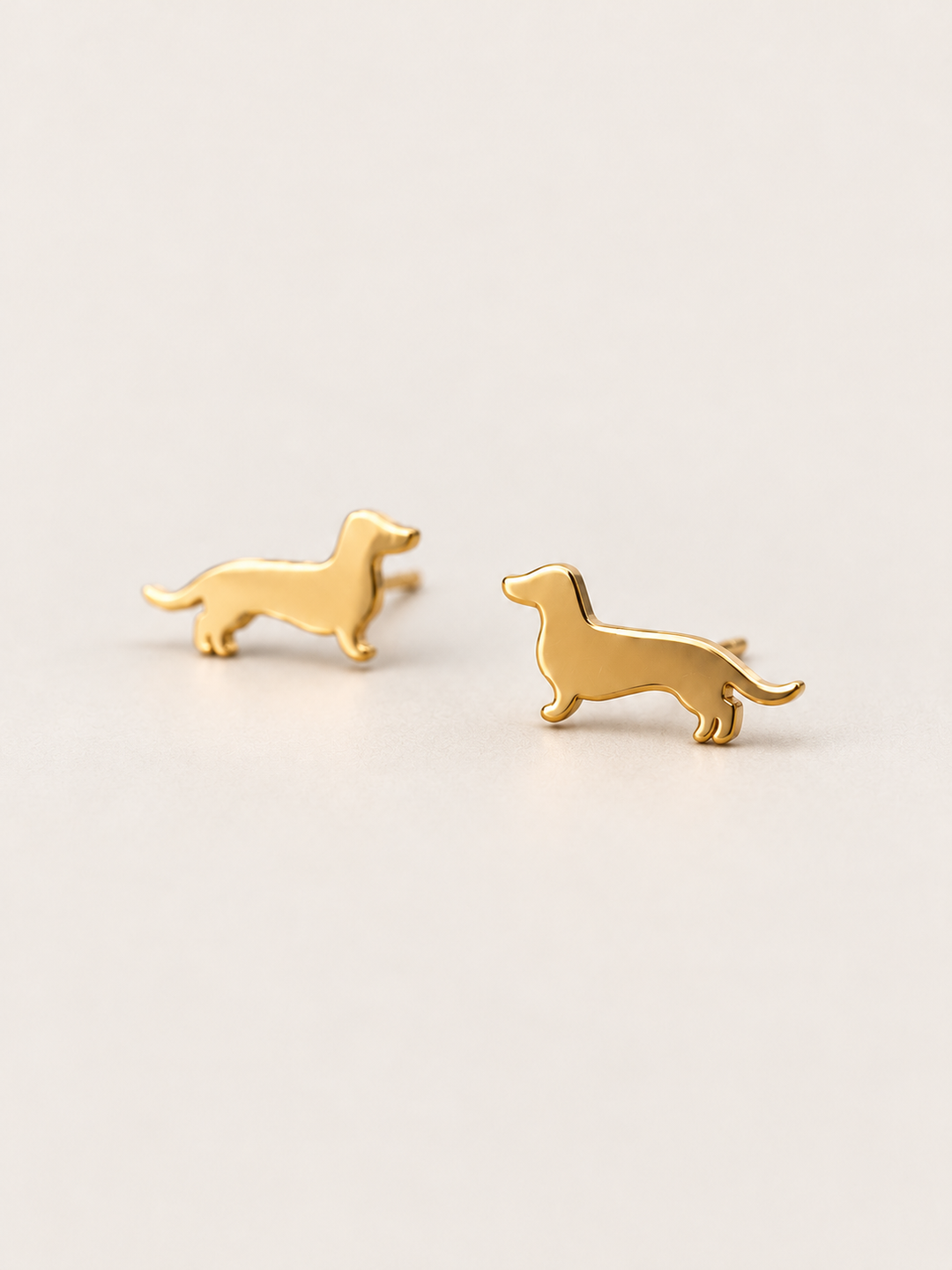 Dachshund Stud Earrings in gold shown angled on a warm neutral background