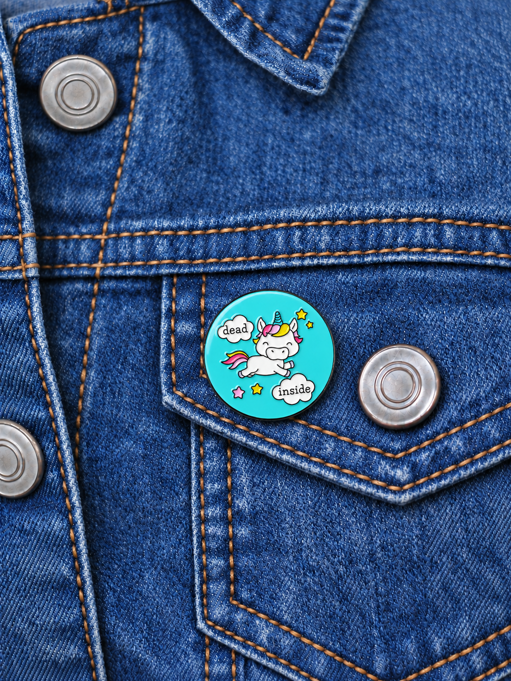 Dead Inside Unicorn Pin displayed on a stonewash denim jacket beside a metal button