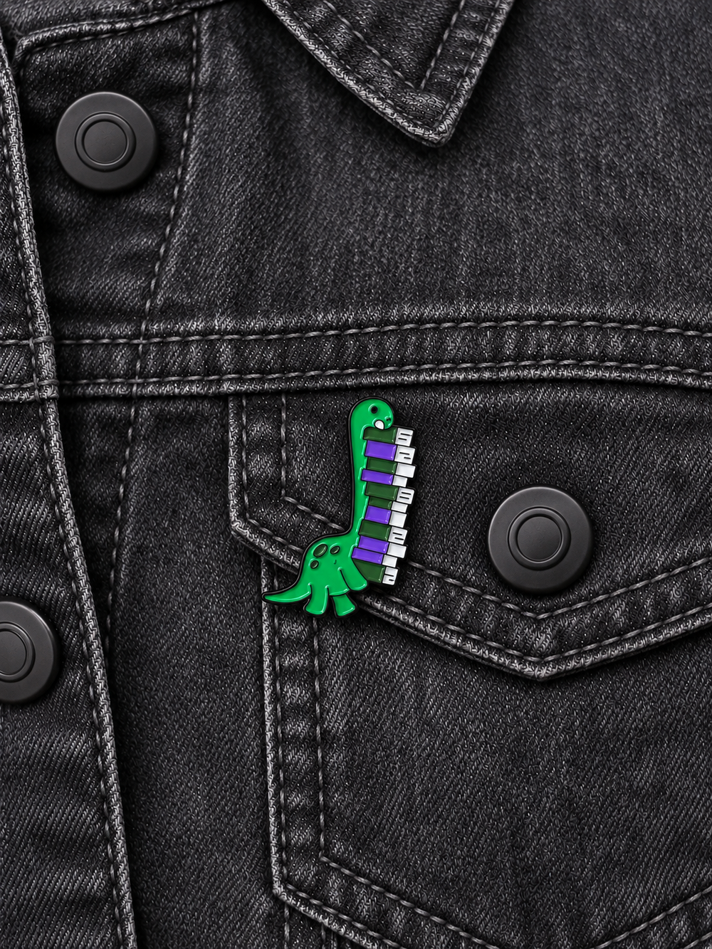 Dinosaur Piano Pin displayed on a charcoal denim jacket beside a metal button