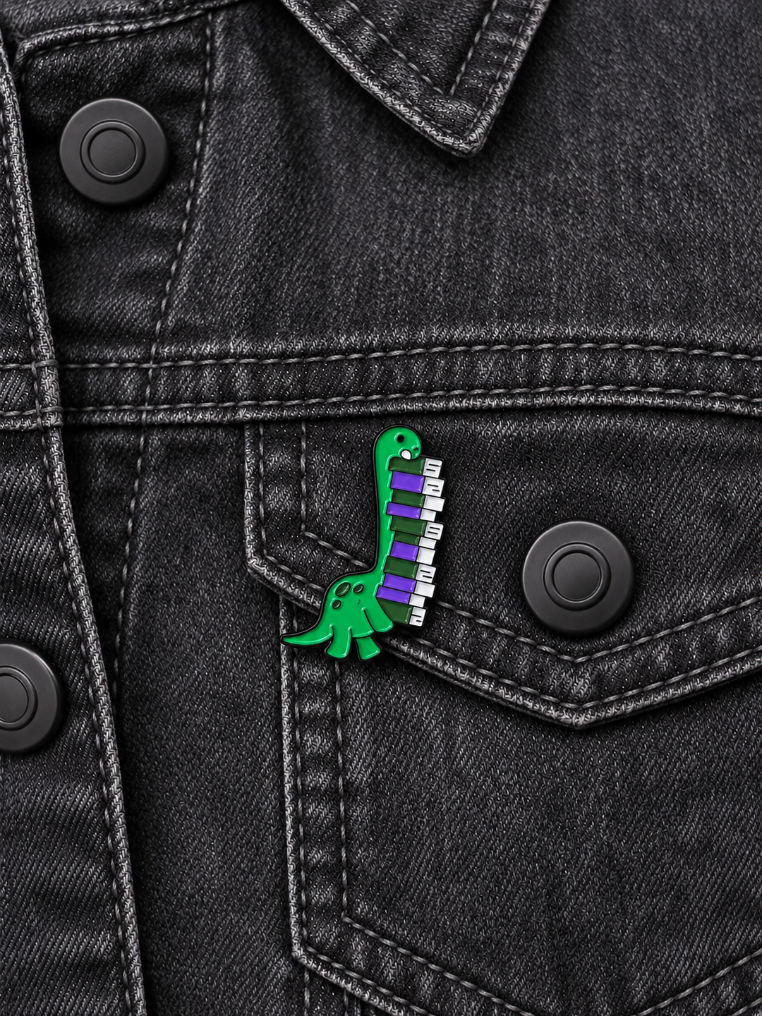 Dinosaur Piano Pin displayed on a charcoal denim jacket beside a metal button