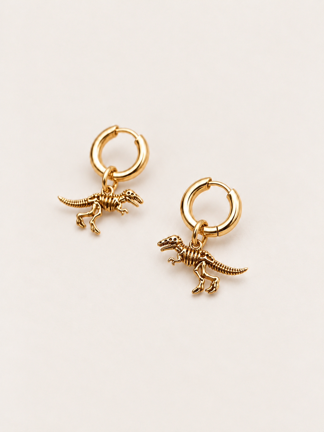 Dinosaur Skeleton Hoop Earrings — gold angle on a warm neutral background