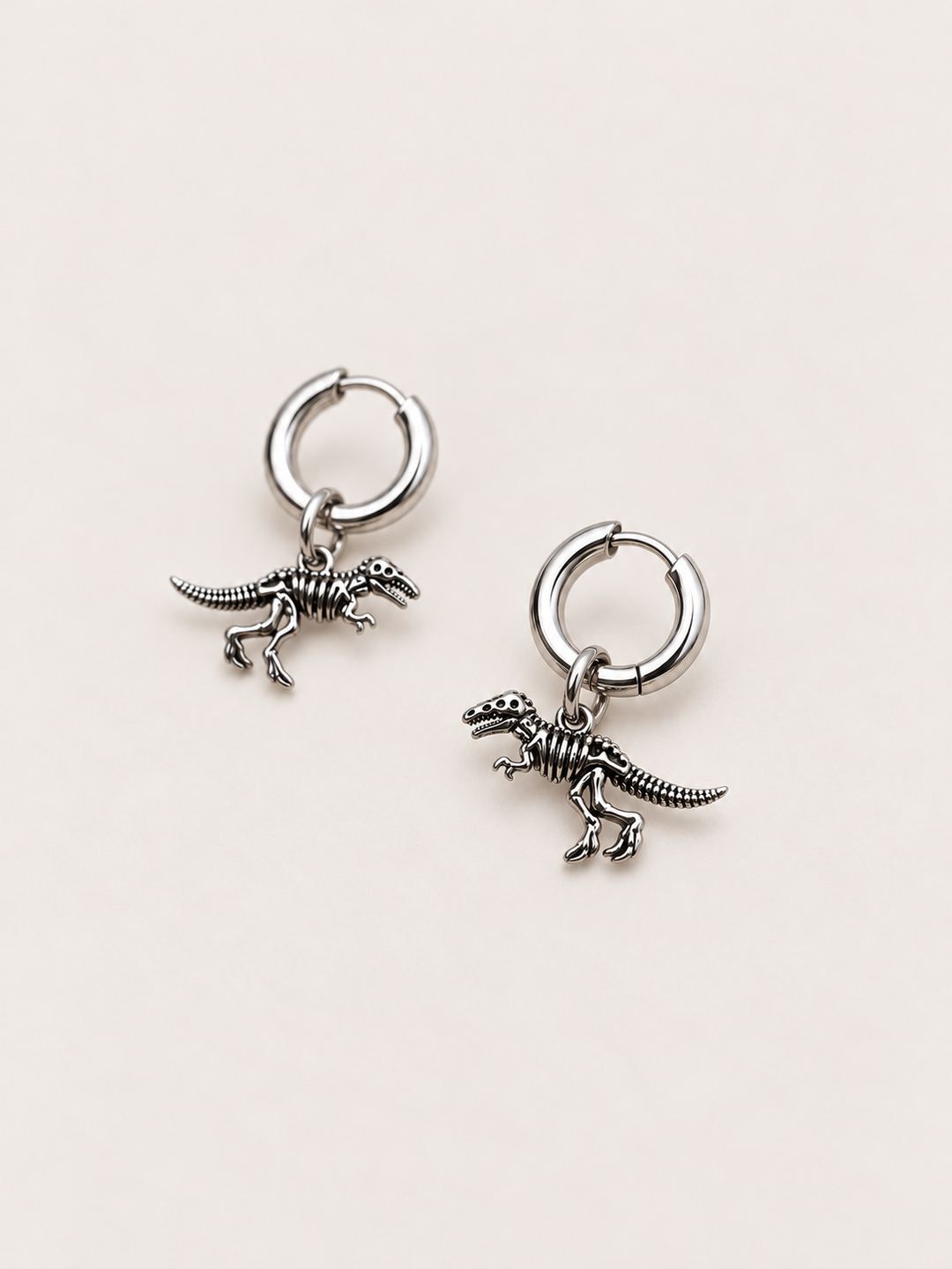 Dinosaur Skeleton Hoop Earrings — silver angle on a warm neutral background
