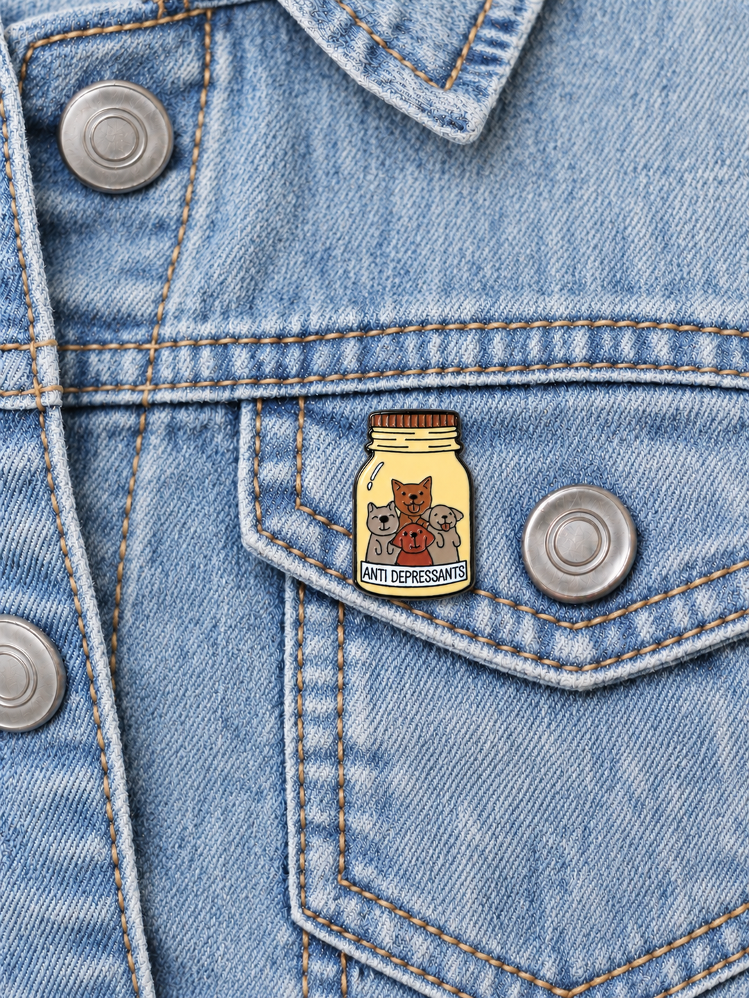 Dogs Antidepressants Bottle Pin displayed on a light-wash denim jacket beside a metal button