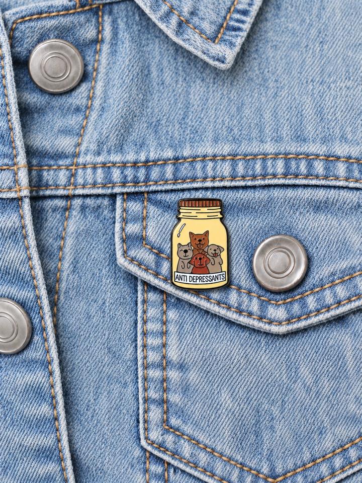 Dogs Antidepressants Bottle Pin displayed on a light-wash denim jacket beside a metal button