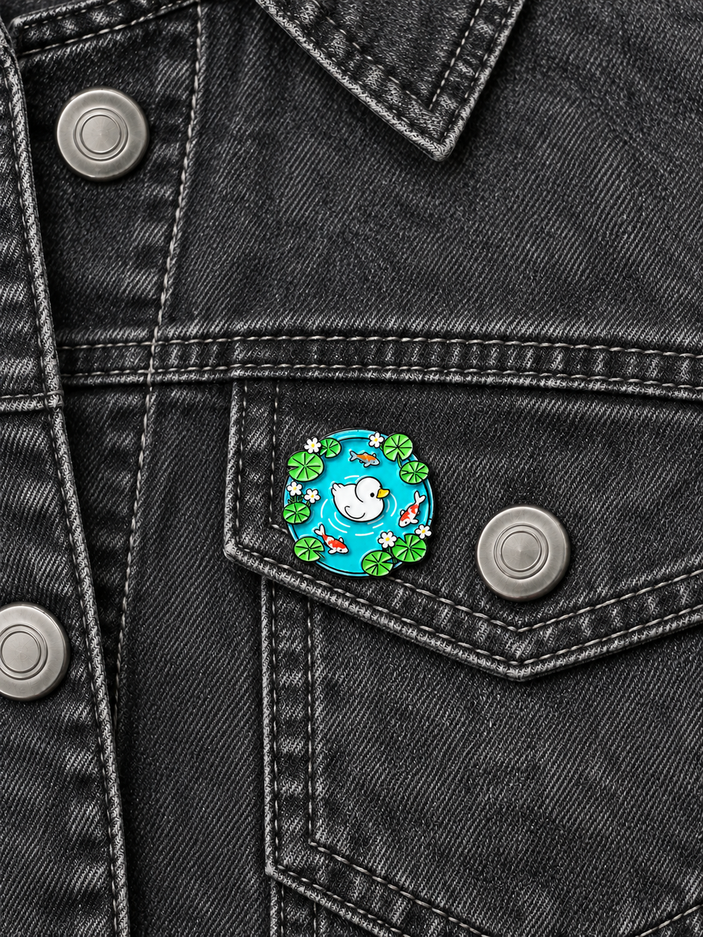 Duck Koi Pond Pin displayed on charcoal denim beside a brushed silver button