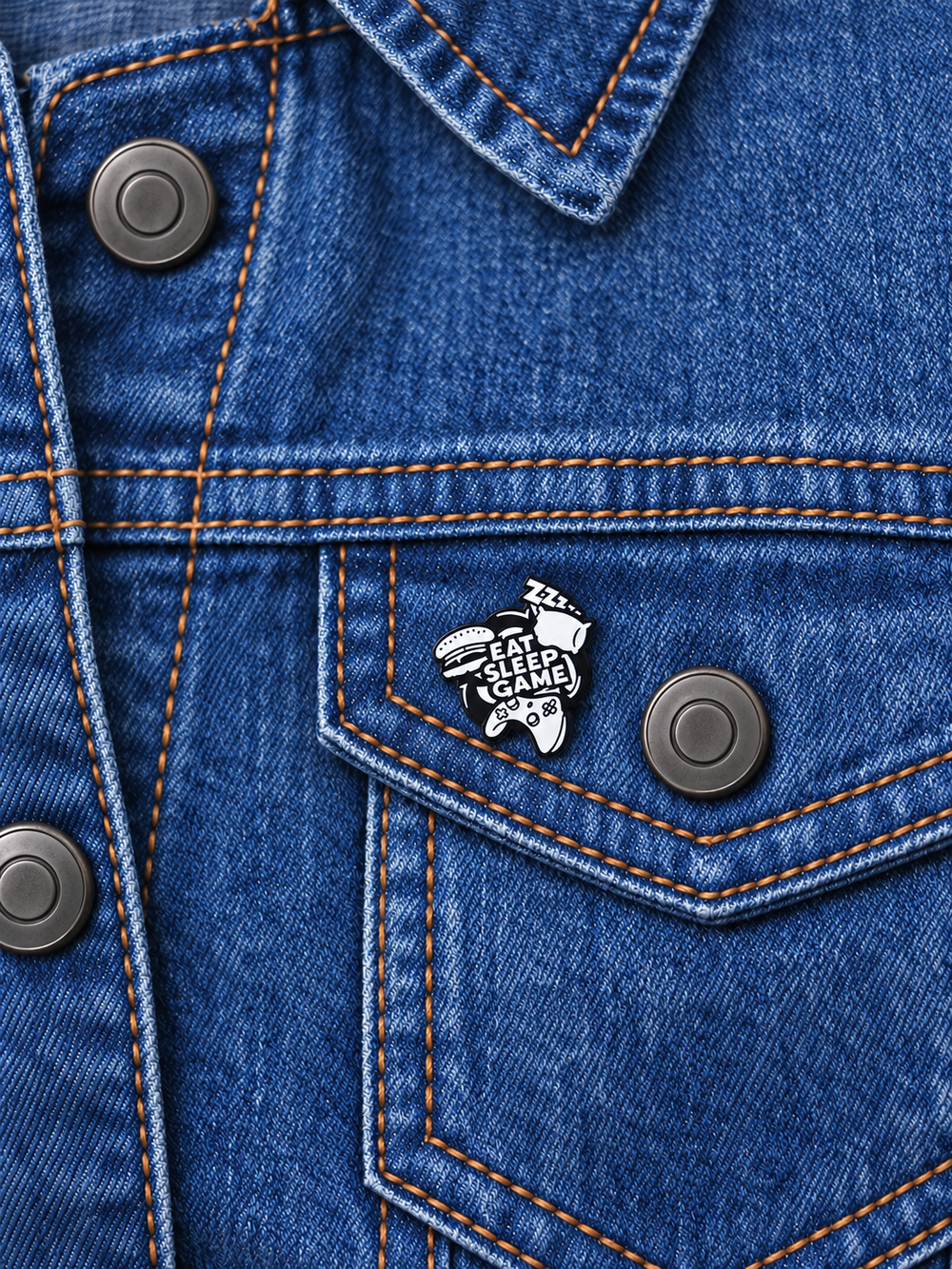 Eat Sleep Game Controller Pin displayed on a faded blue denim jacket beside a metal button