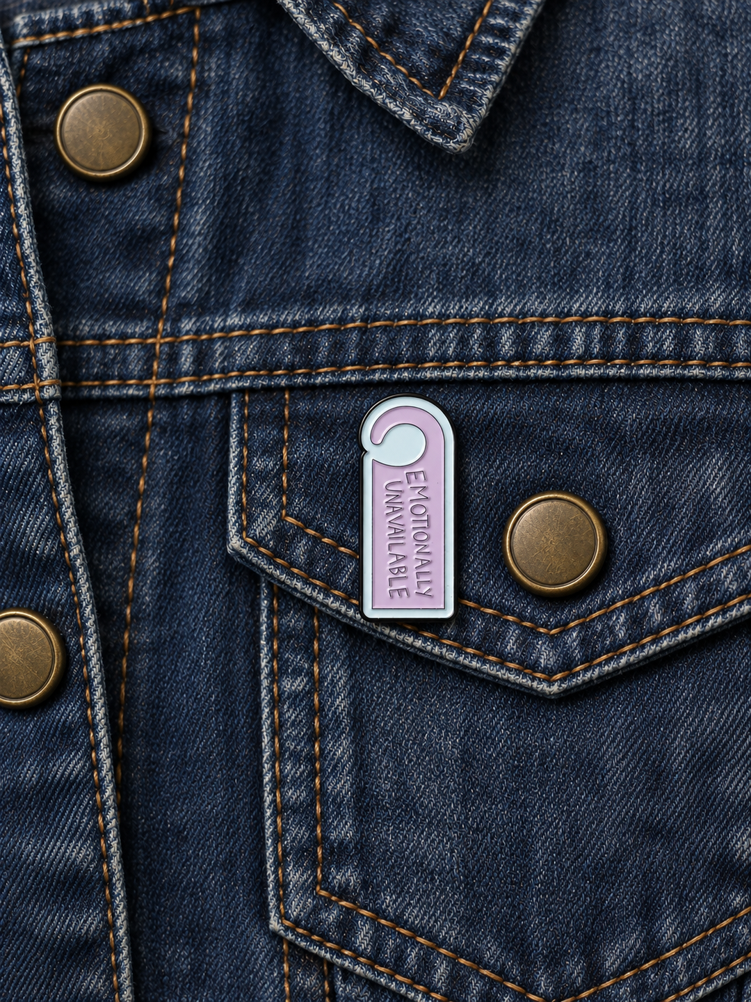 Emotionally Unavailable Door Hanger Pin displayed on a dark indigo denim jacket beside a metal button