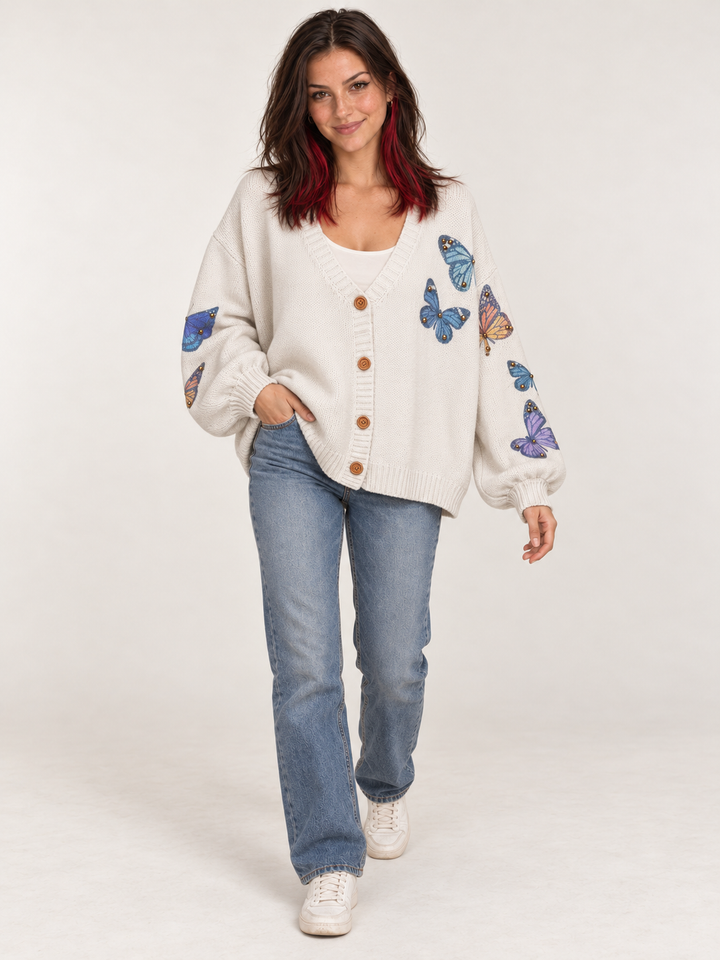 Full-body view of model wearing ivory butterfly cardigan with blue jeans and cream sneakers