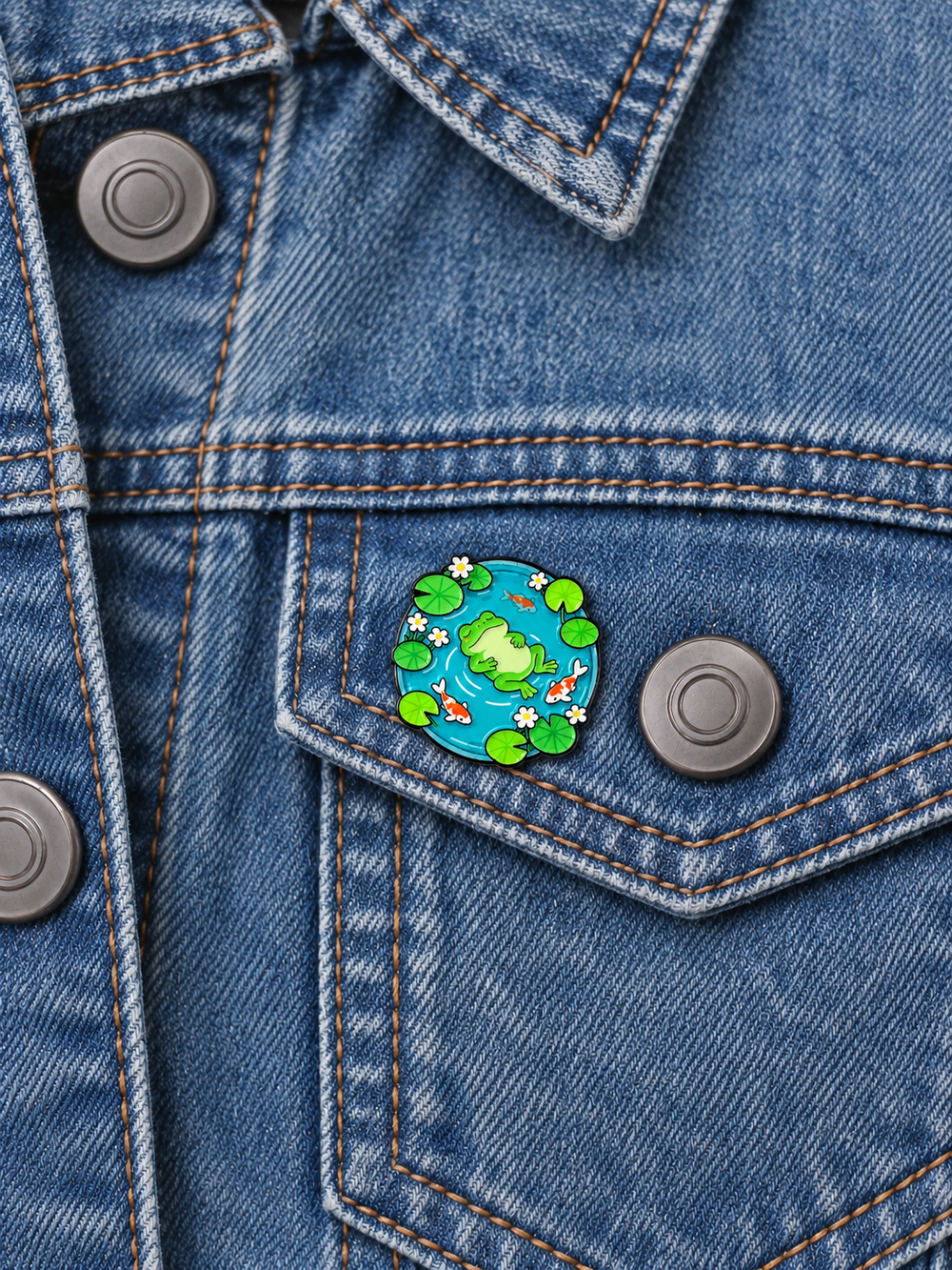 Frog and Koi Pond Pin displayed on a faded blue denim jacket beside a metal button
