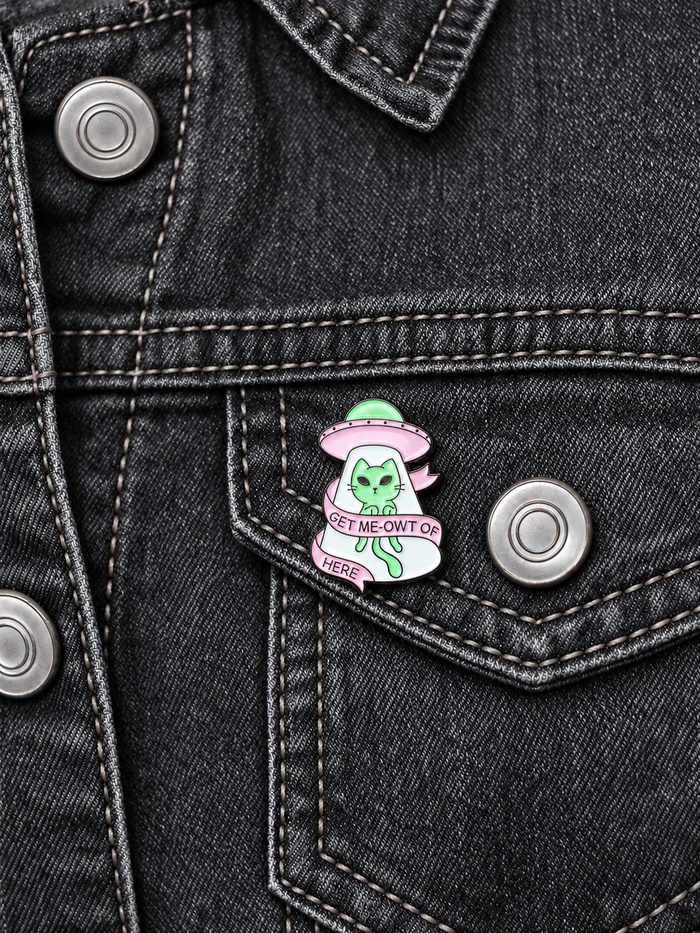 Get Me-Owt of Here Alien Cat Pin displayed on charcoal denim beside a metal button