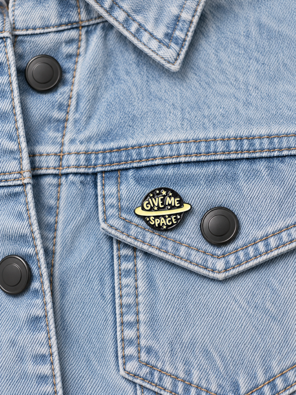 Give Me Space Planet Pin displayed on a light-wash denim jacket beside a matte black metal button