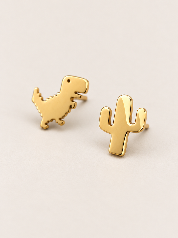 Gold Dinosaur and Cactus Stud Earrings shown angled on a warm neutral background