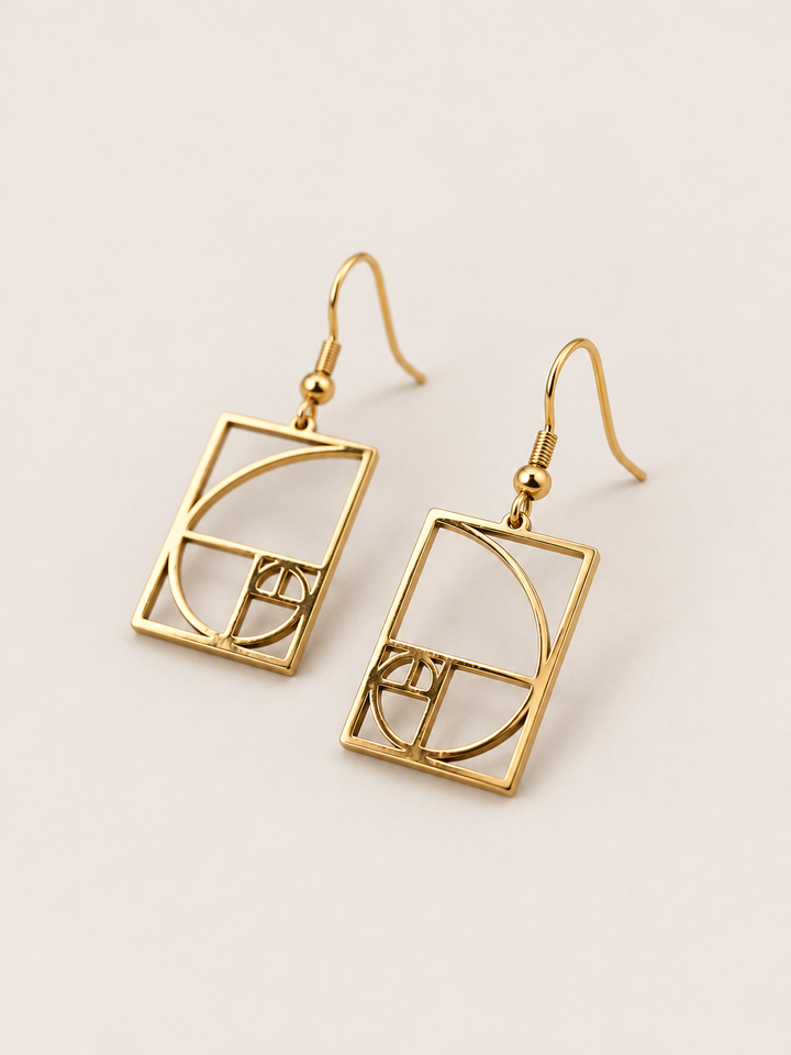 Gold Golden Ratio Spiral Drop Earrings shown angled on a warm neutral background