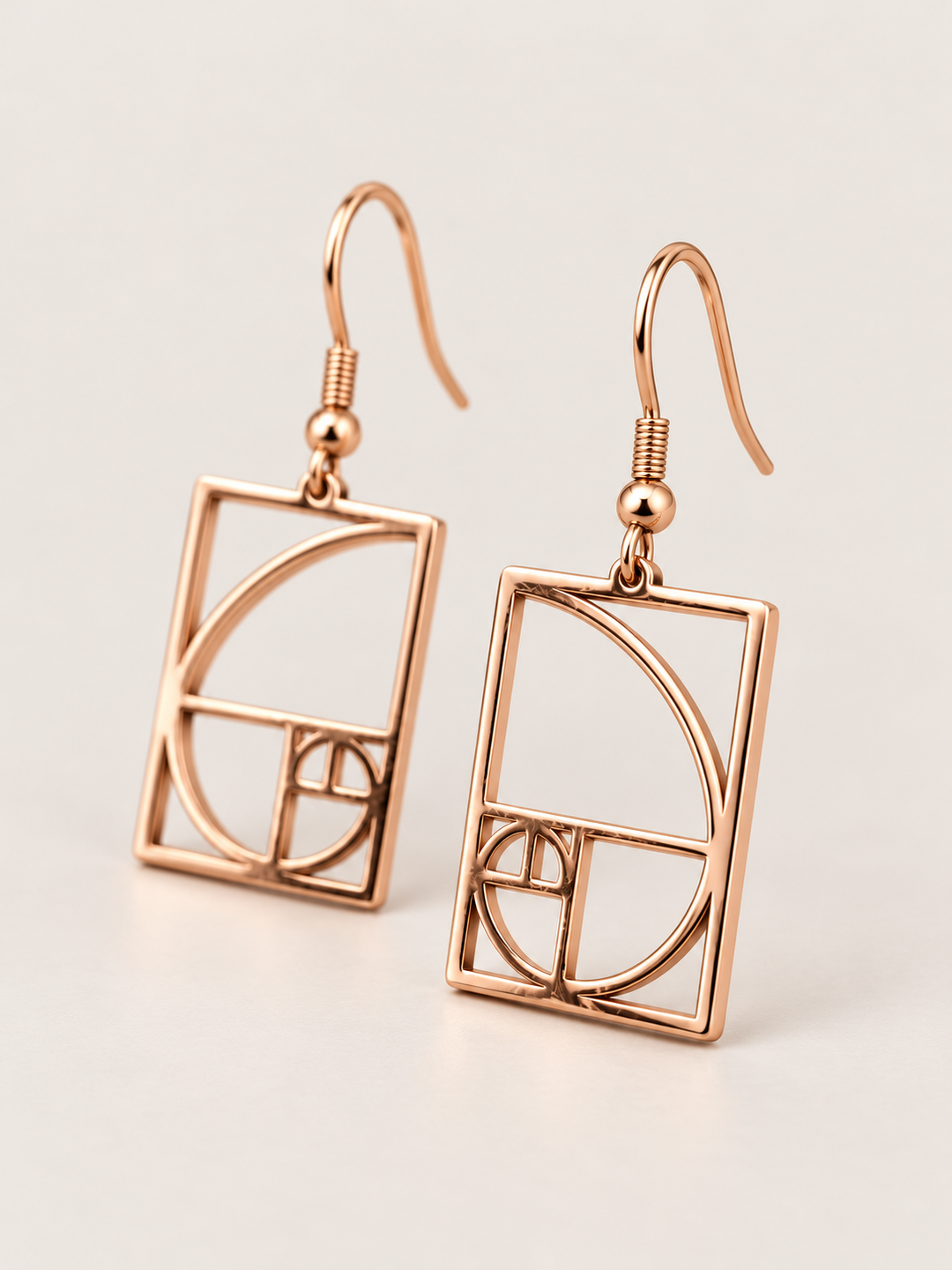 Rose gold Golden Ratio Spiral Drop Earrings shown angled on a warm neutral background