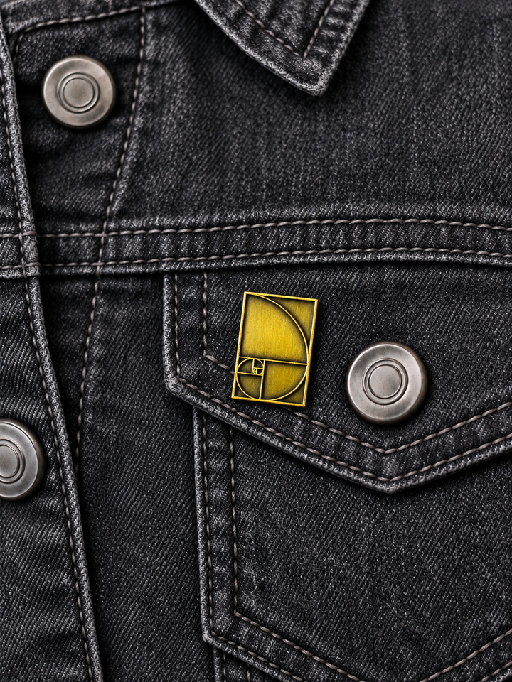 Golden Ratio Spiral Pin displayed on a charcoal denim jacket beside a metal button