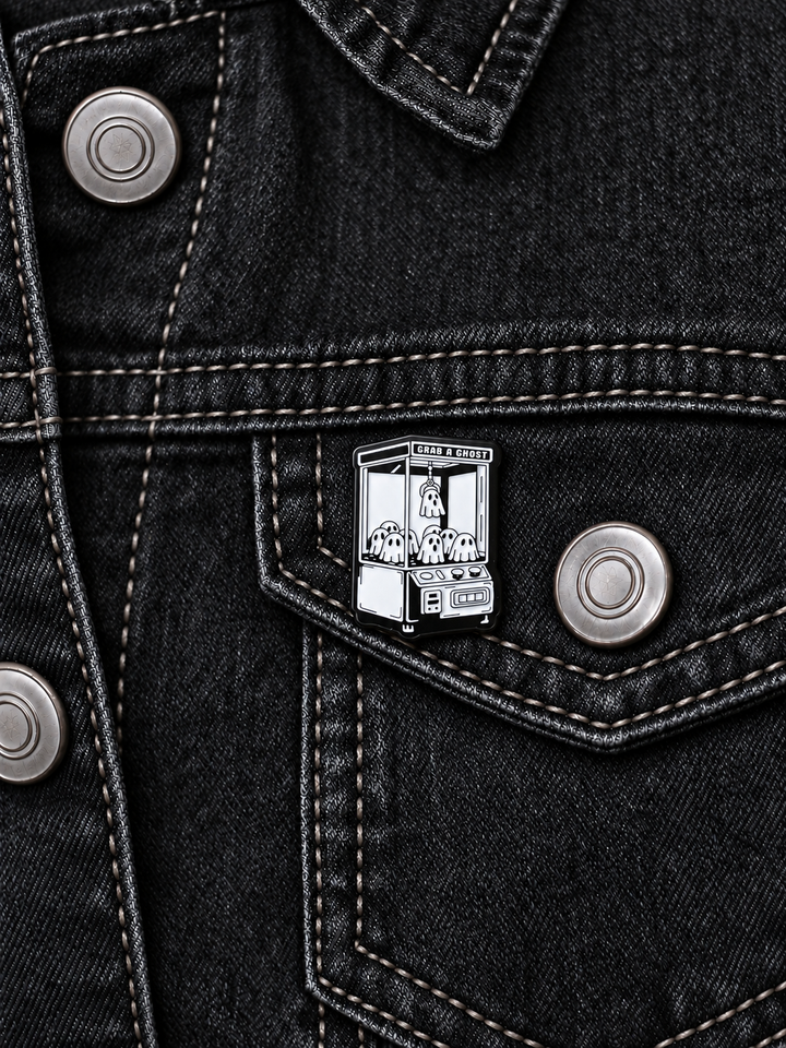 Grab a Ghost Claw Machine Pin displayed on black denim beside a metal button