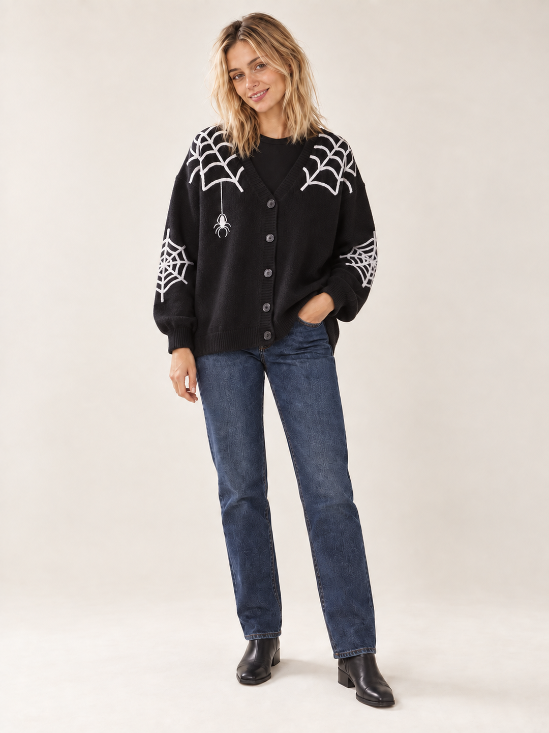 Full body front view of model wearing black Halloween spiderweb cardigan with dark blue jeans