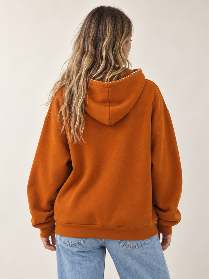 Model wearing burnt orange embroidered pumpkin hoodie, back view