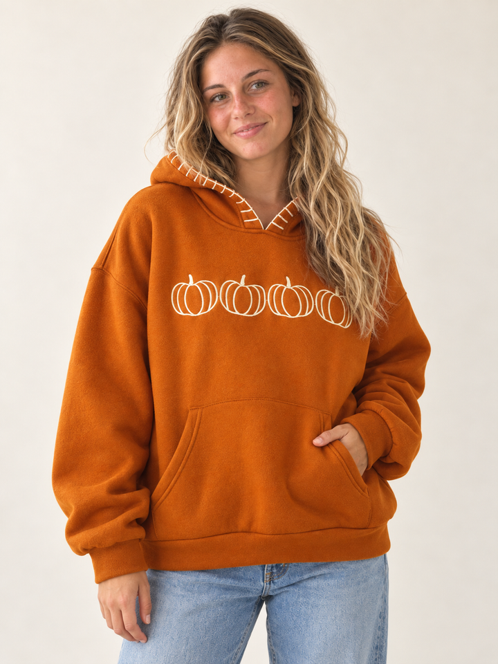 Model wearing burnt orange embroidered pumpkin hoodie, front view