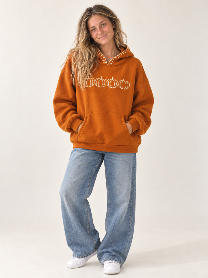 Model wearing burnt orange embroidered pumpkin hoodie, full-body front view