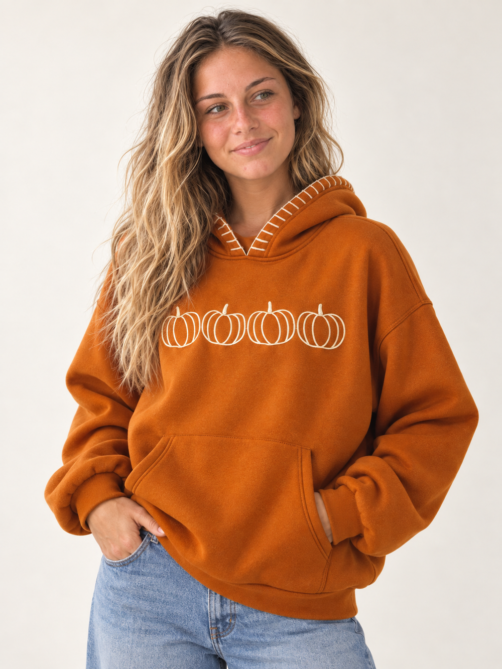 Model wearing burnt orange embroidered pumpkin hoodie, three-quarter view
