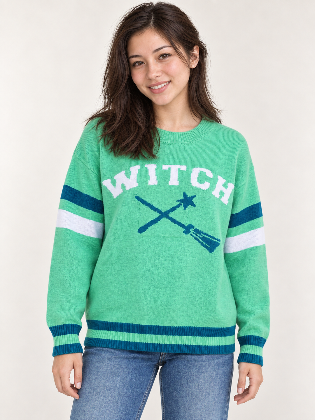 front view of model wearing green Halloween WITCH sweater with teal and white striped details