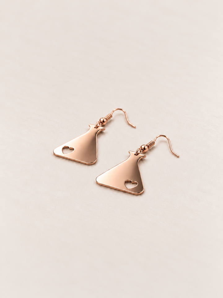 Rose Gold Heart Flask Drop Earrings lying flat at an angle on a warm neutral background