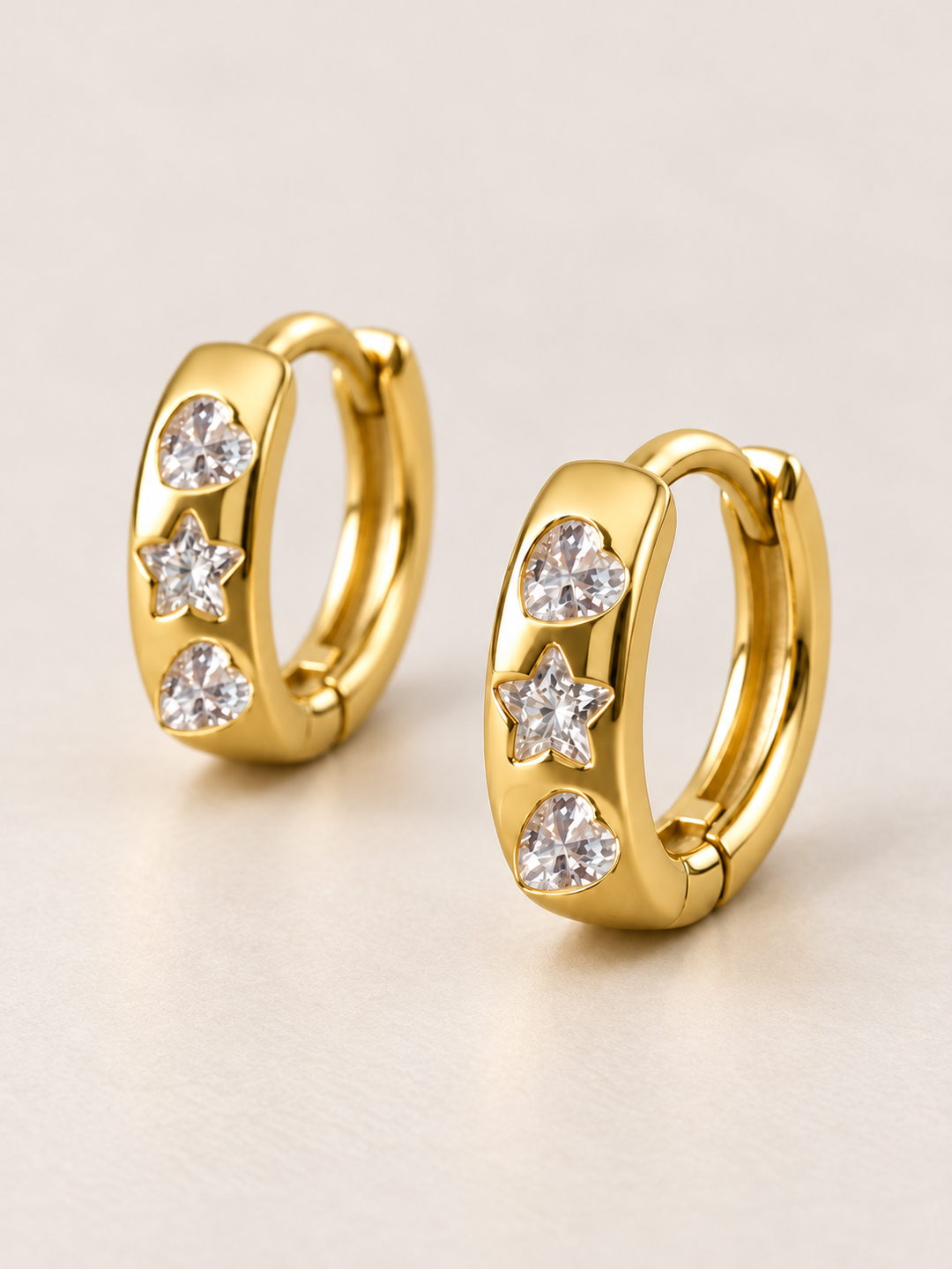 Heart and Star Huggie Earrings shown angled on a warm neutral background