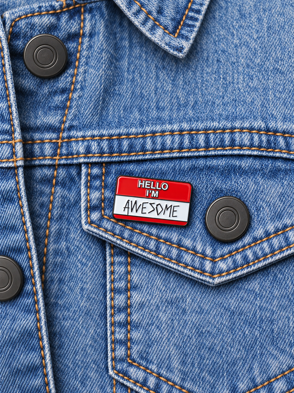 Hello I'm Awesome Name Tag Pin displayed on a pale stonewash denim jacket beside a metal button