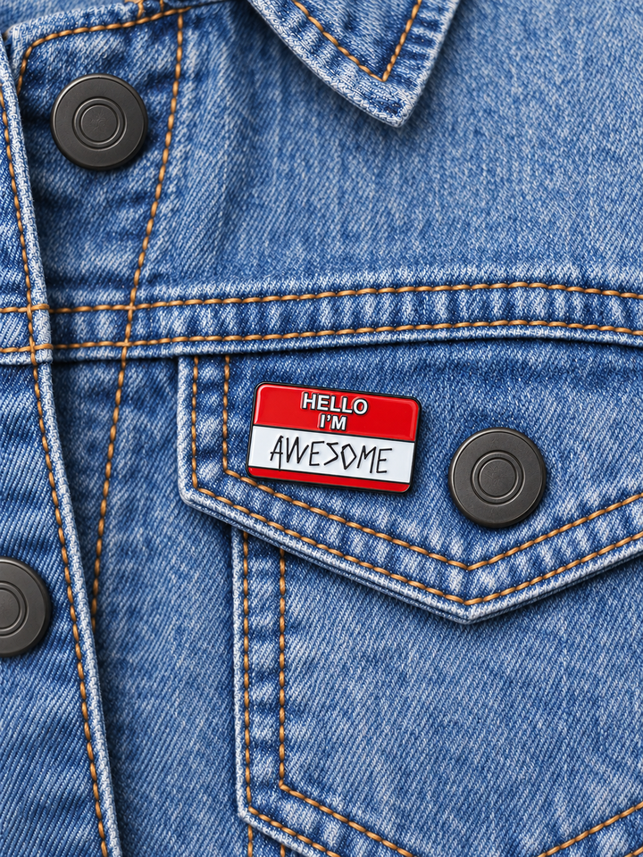 Hello I'm Awesome Name Tag Pin displayed on a pale stonewash denim jacket beside a metal button