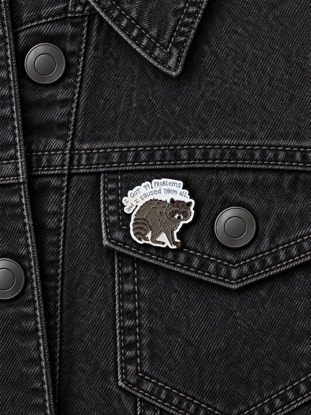 I Got 99 Problems Raccoon Pin displayed on a black denim jacket beside a metal button