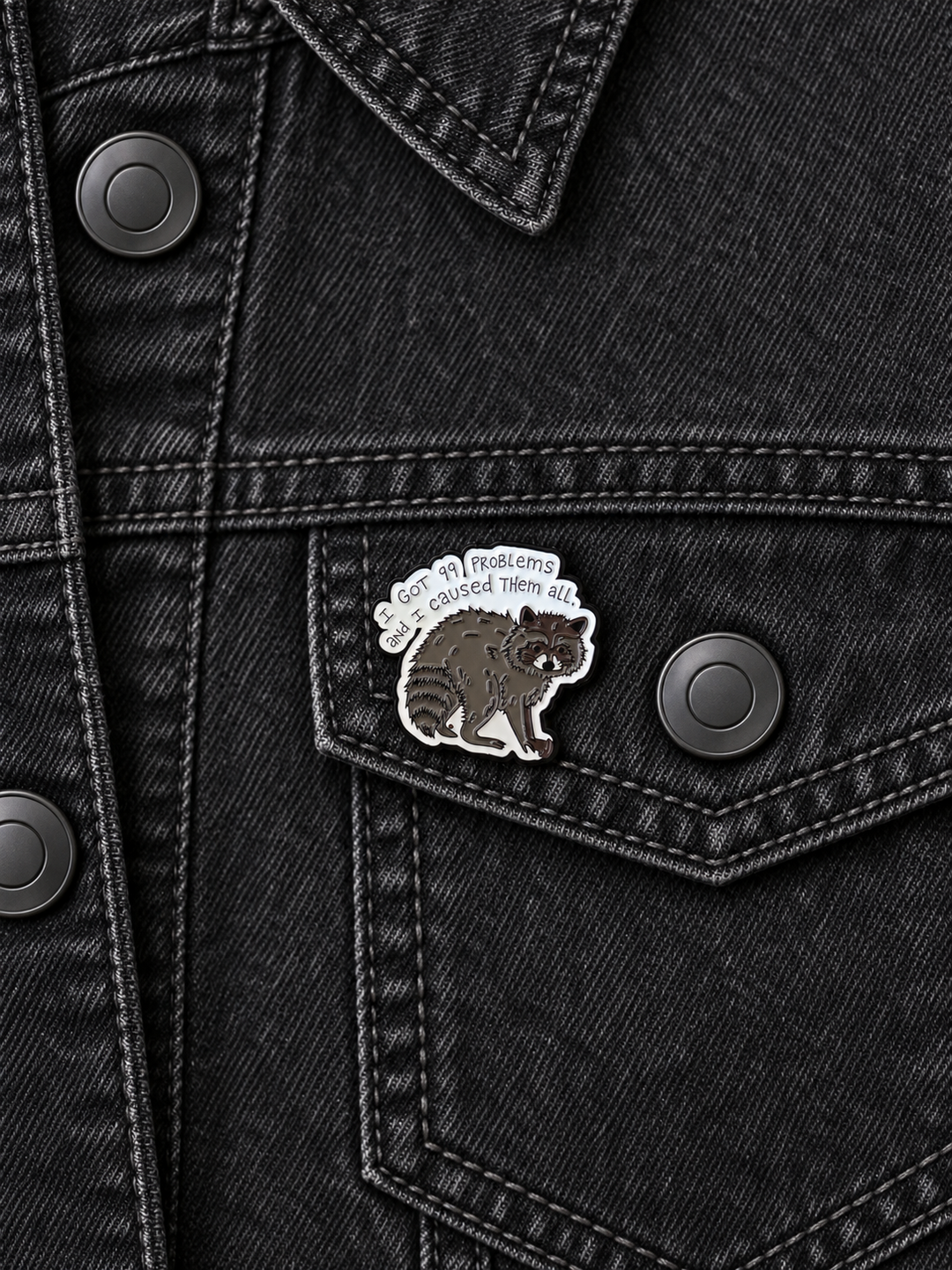 I Got 99 Problems Raccoon Pin displayed on a black denim jacket beside a metal button
