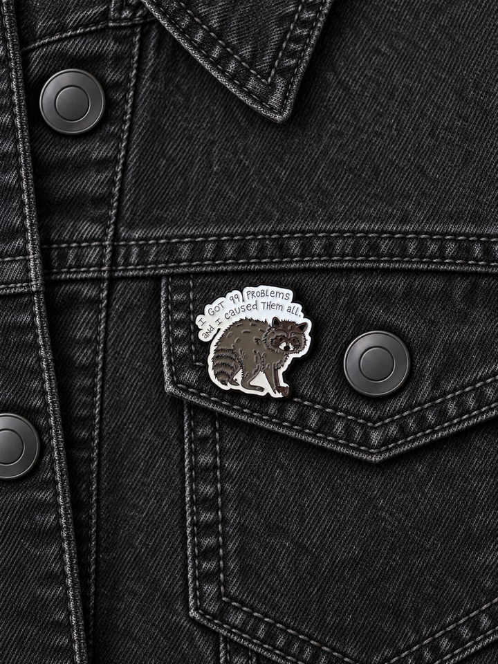 I Got 99 Problems Raccoon Pin displayed on a black denim jacket beside a metal button
