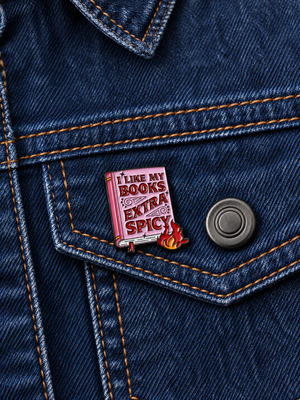 I Like My Books Extra Spicy Pin displayed on a dark indigo denim jacket beside a metal button