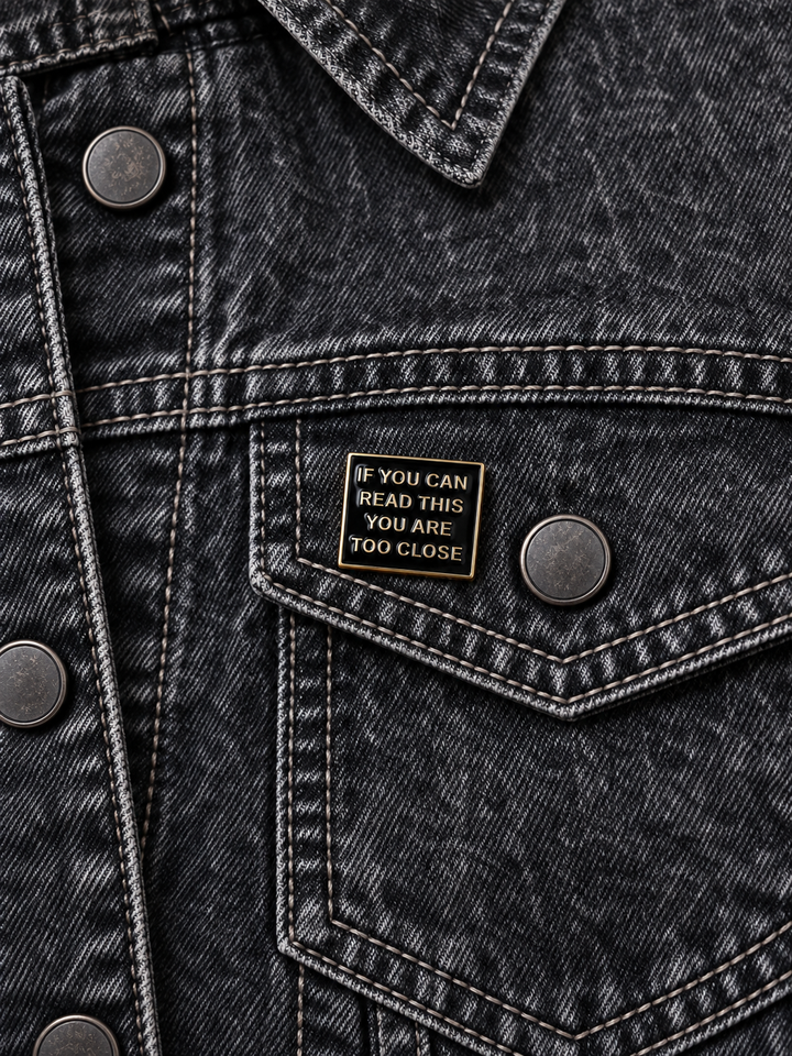 If You Can Read This Too Close Pin displayed on a black acid-wash denim jacket beside a metal button
