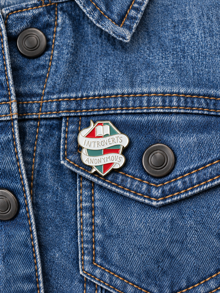 Introverts Anonymous Book Pin displayed on a blue denim jacket beside a metal button