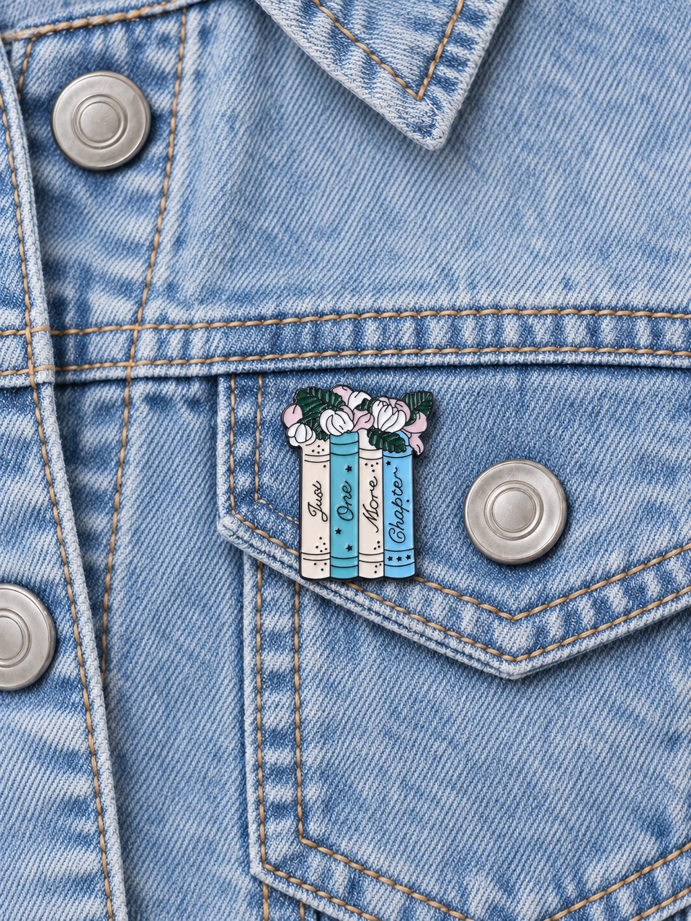 Just One More Chapter Pin displayed on a light-wash denim jacket beside a metal button