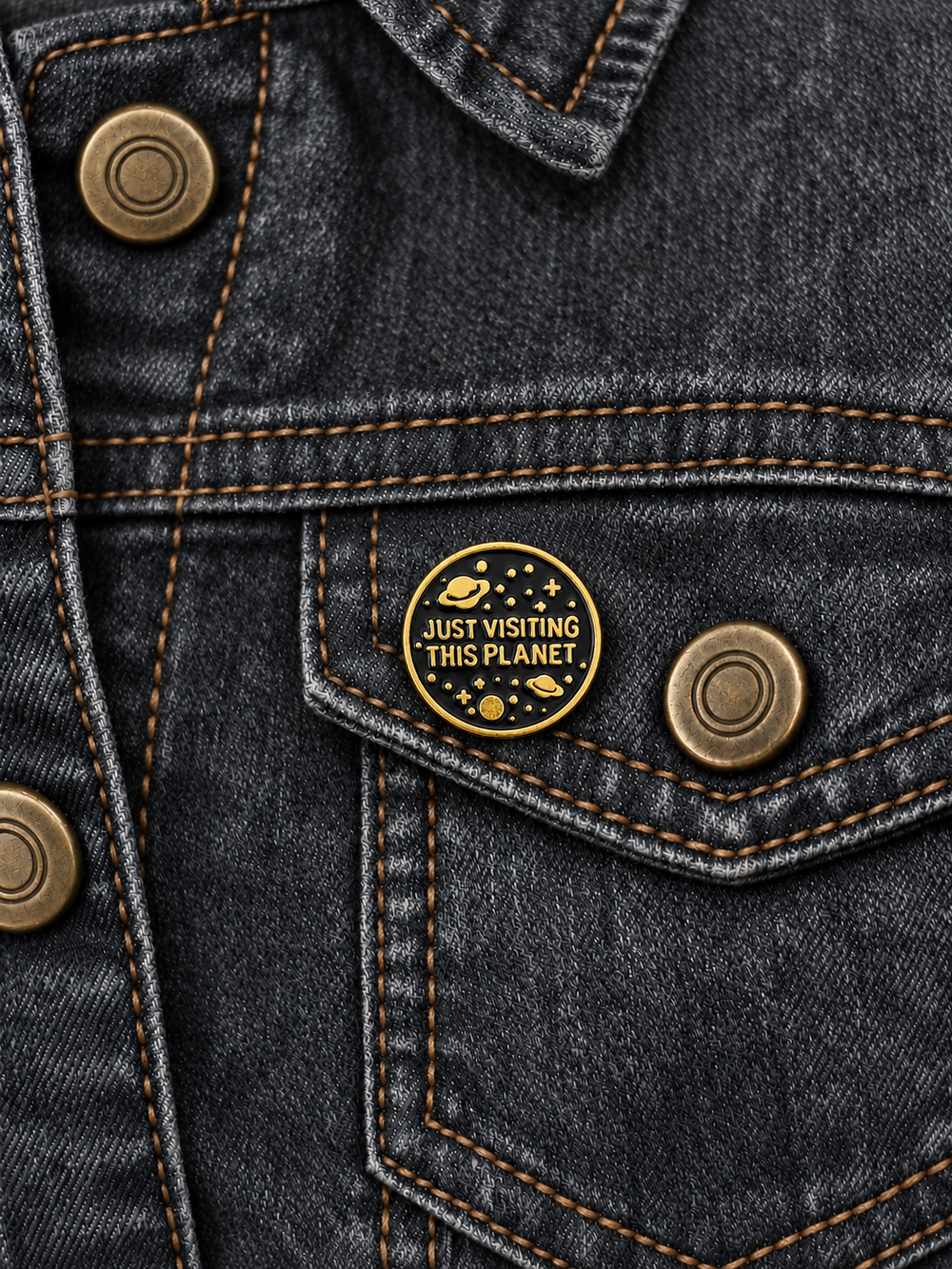 Just Visiting This Planet Pin displayed on charcoal denim beside an antiqued brass button