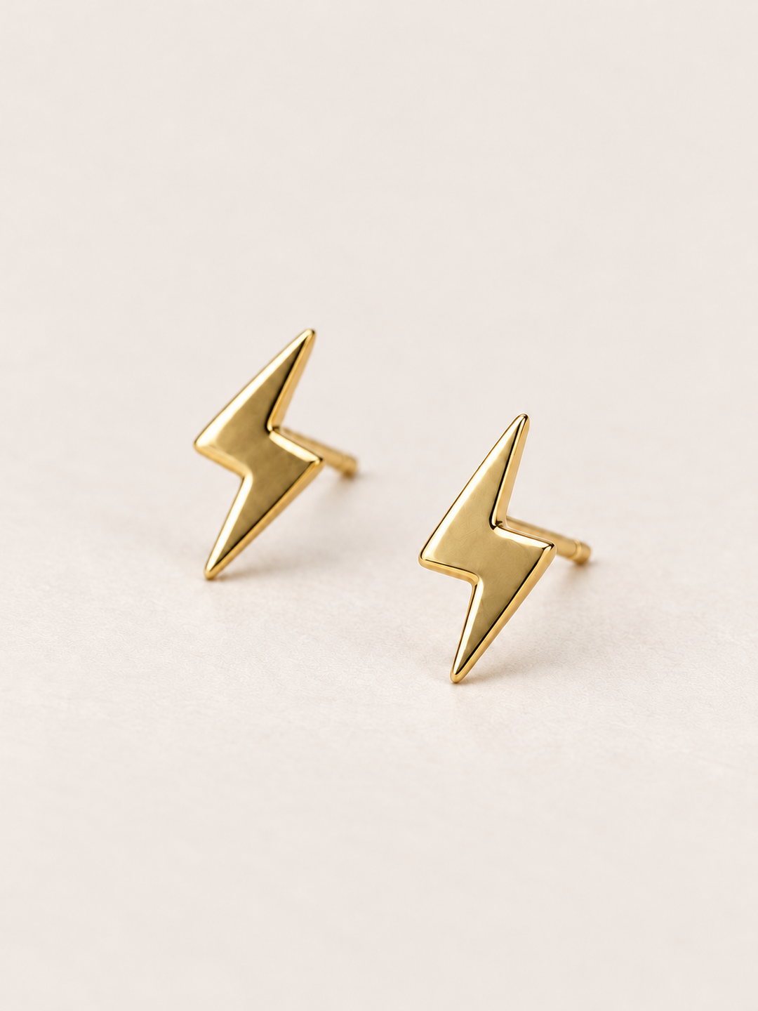 Gold Lightning Bolt Earrings angled on a warm neutral background