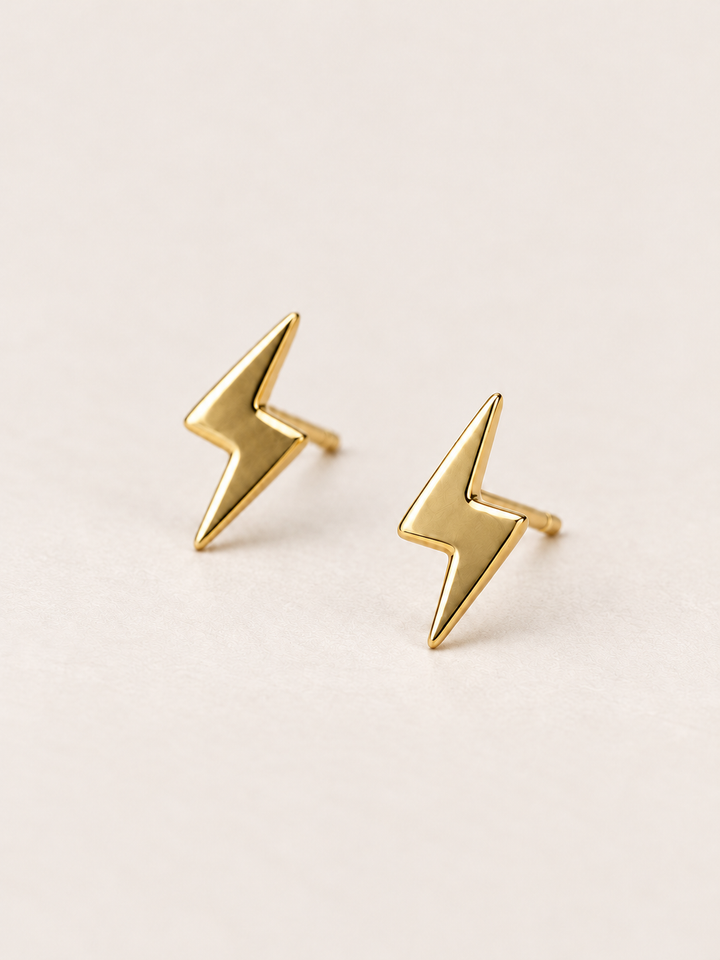 Gold Lightning Bolt Earrings angled on a warm neutral background