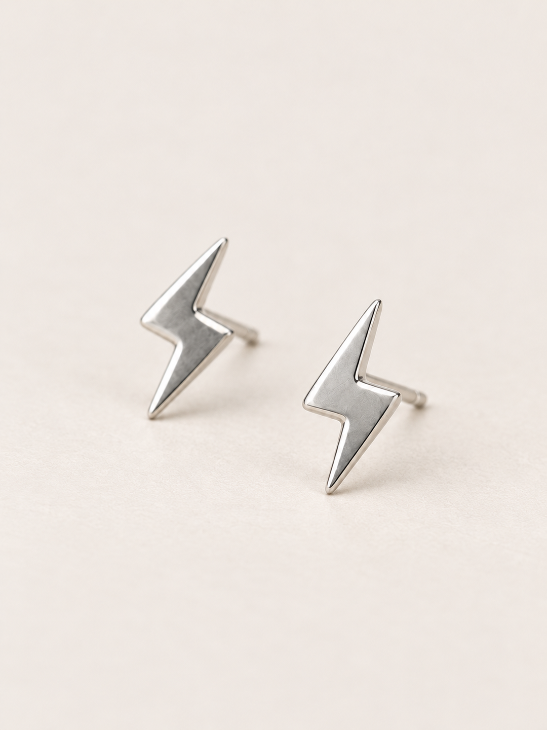 Silver Lightning Bolt Earrings angled on a warm neutral background
