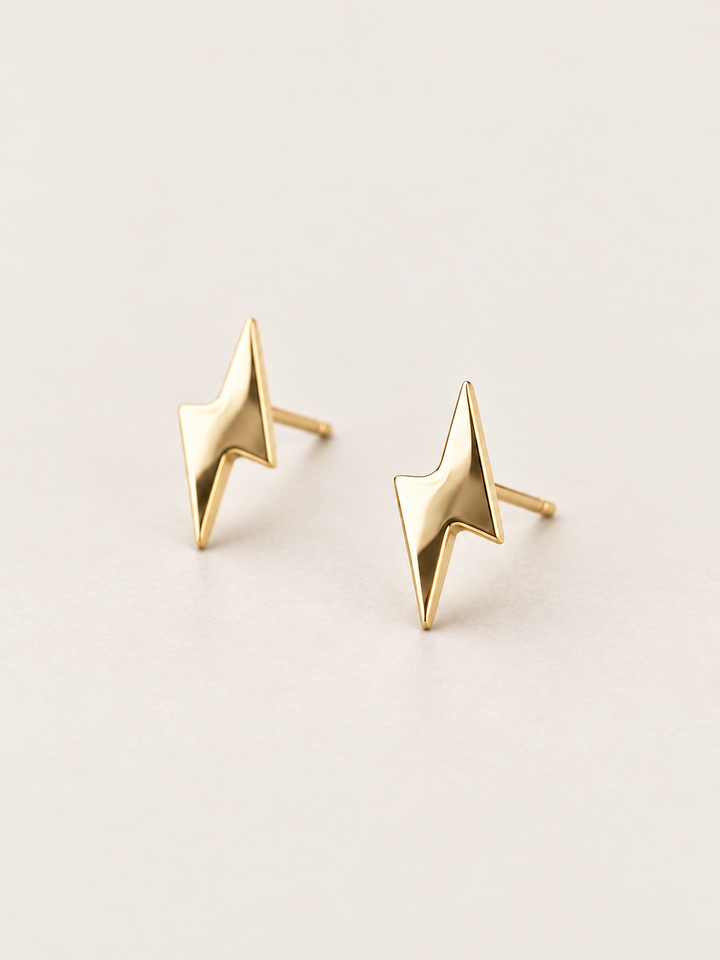 Gold Lightning Bolt Stud Earrings shown angled on a warm neutral background