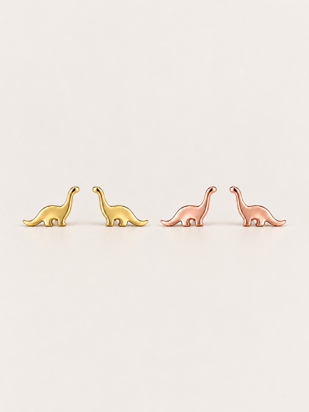 Long Neck Dinosaur Stud Earrings in gold and rose gold shown on a warm neutral background