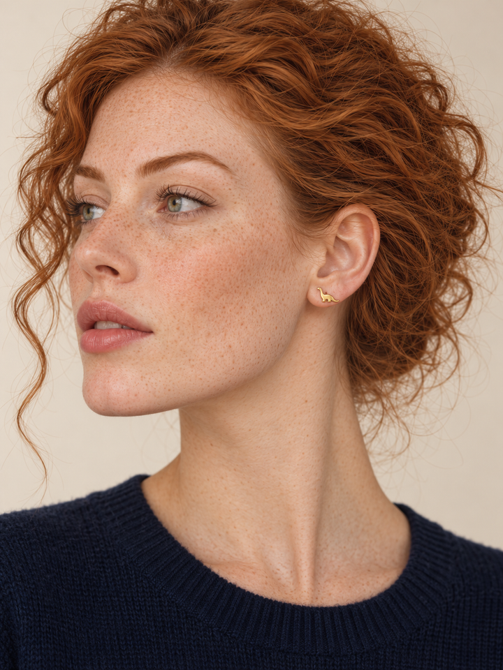 Long Neck Dinosaur Stud Earrings in gold worn on the viewer-right ear