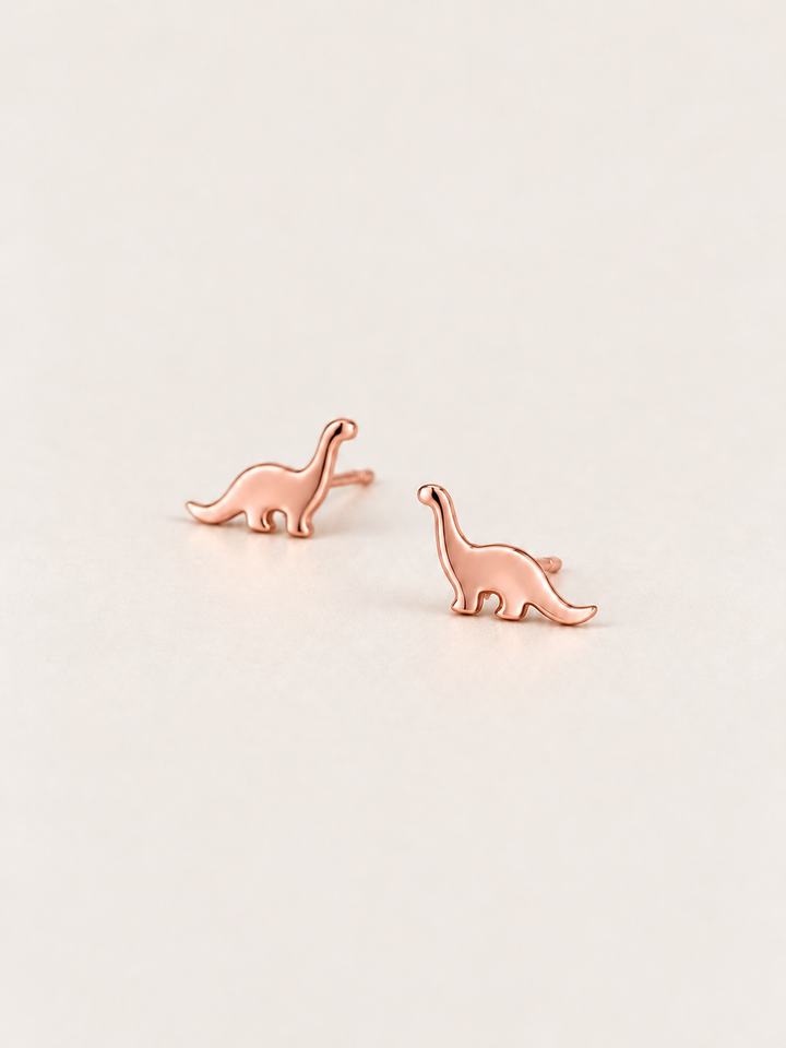 Long Neck Dinosaur Stud Earrings in rose gold shown angled on a warm neutral background