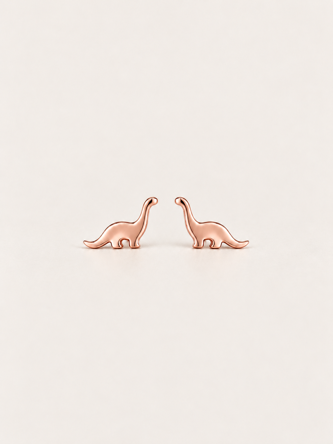 Long Neck Dinosaur Stud Earrings in rose gold on a warm neutral background