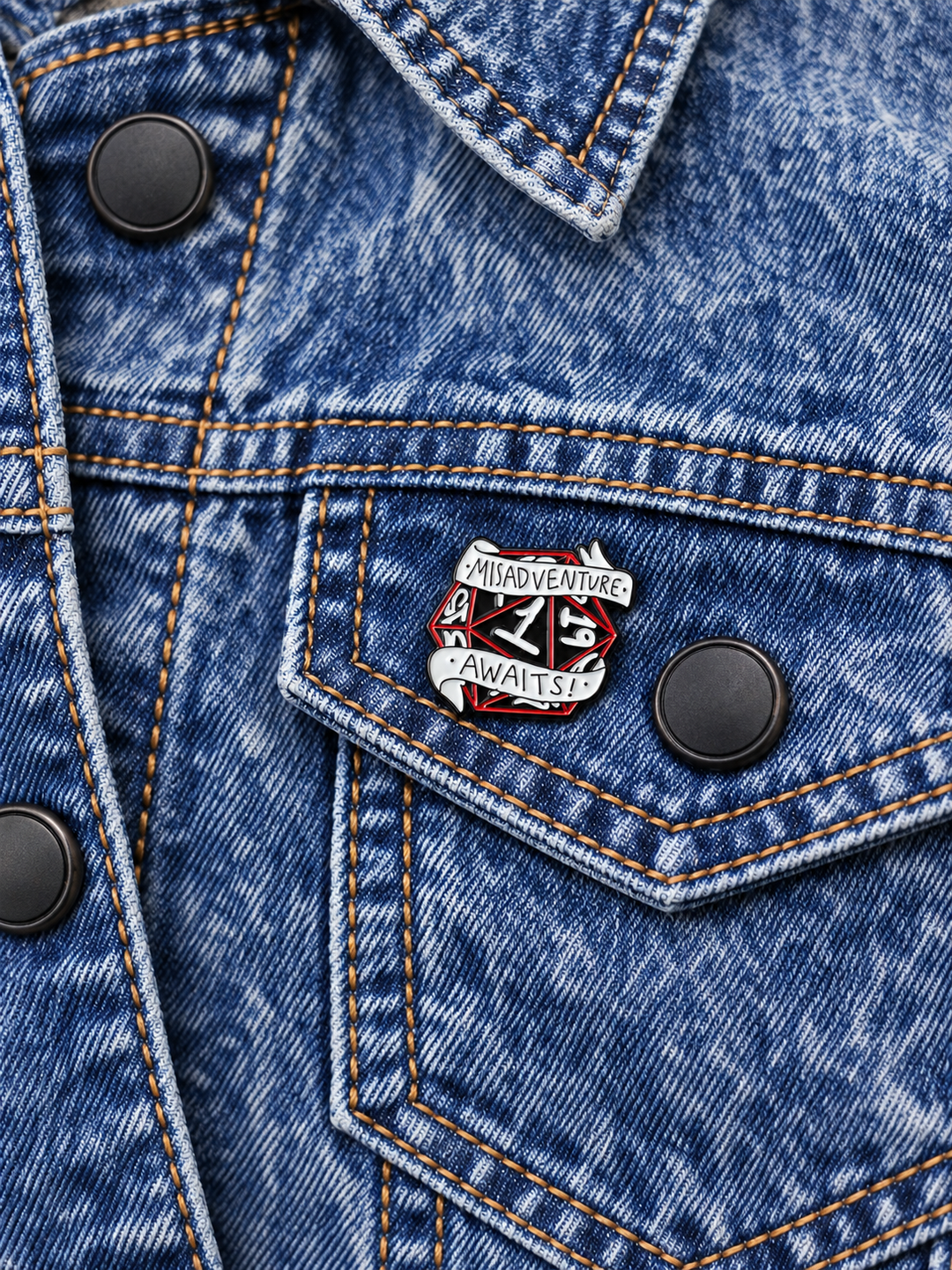 Misadventure Awaits D20 Pin displayed on acid-wash denim beside a metal button