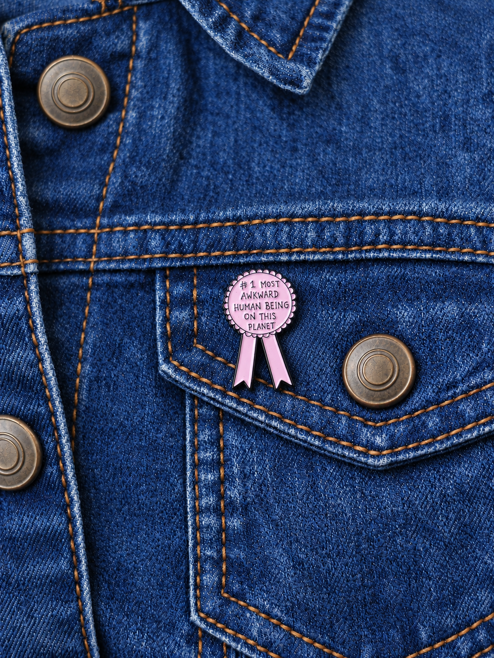 Most Awkward Human Being Award Ribbon Pin displayed on a dark indigo denim jacket beside a metal button