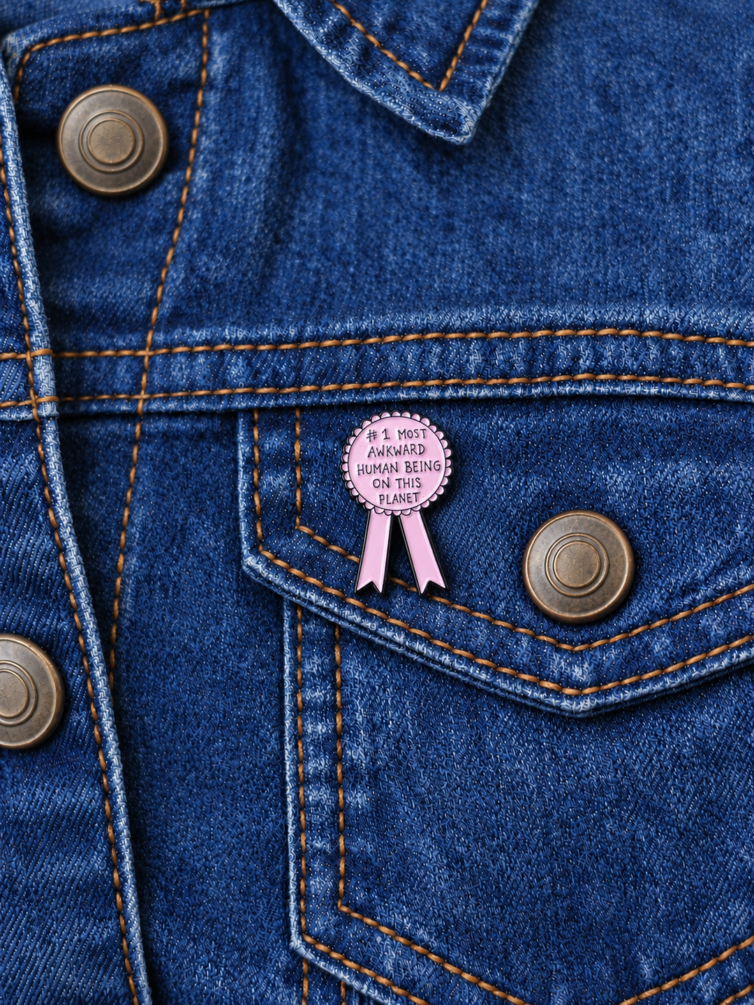 Most Awkward Human Being Award Ribbon Pin displayed on a dark indigo denim jacket beside a metal button