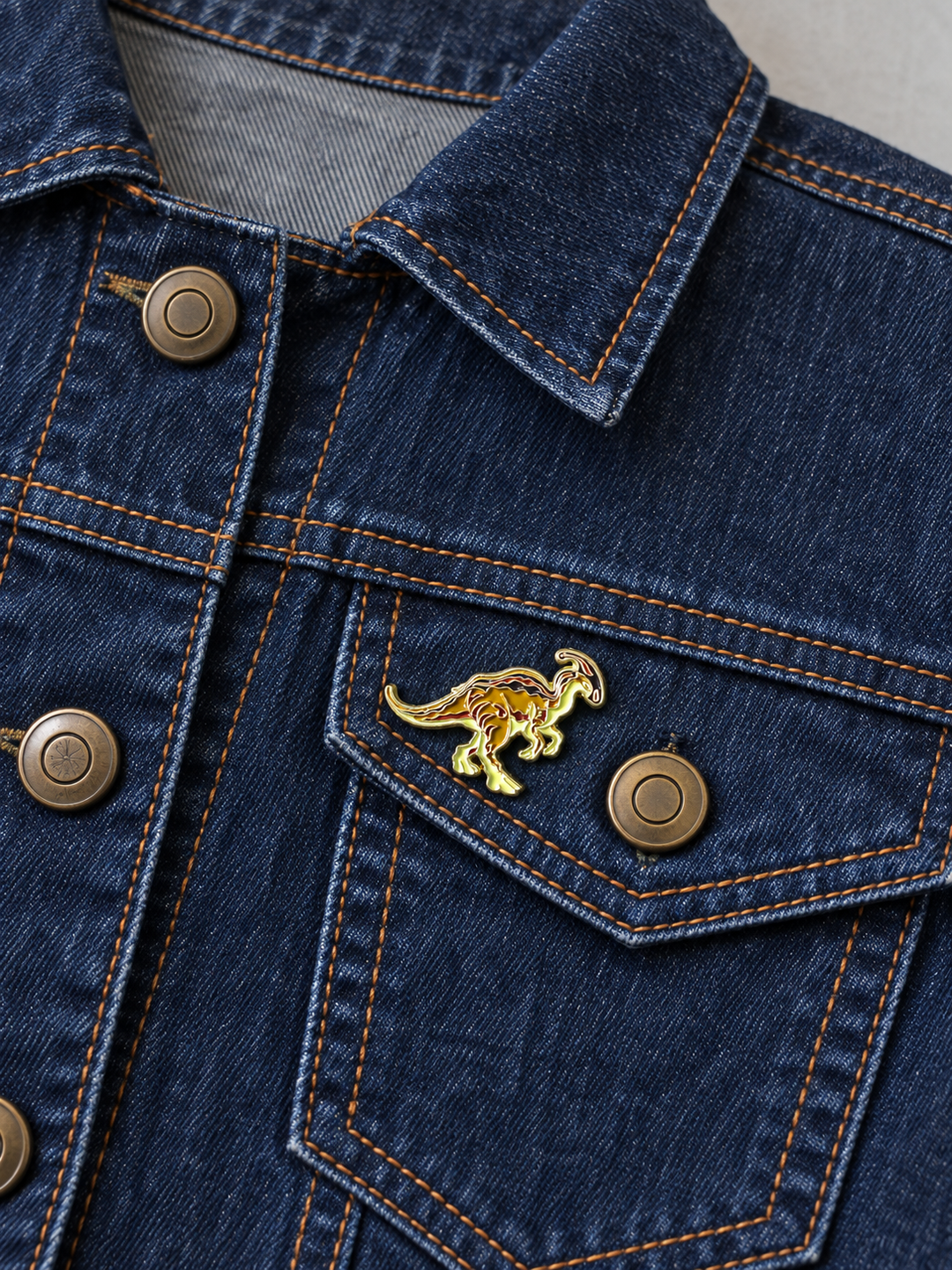 Parasaurolophus Dinosaur Pin displayed on a dark indigo denim jacket beside a metal button